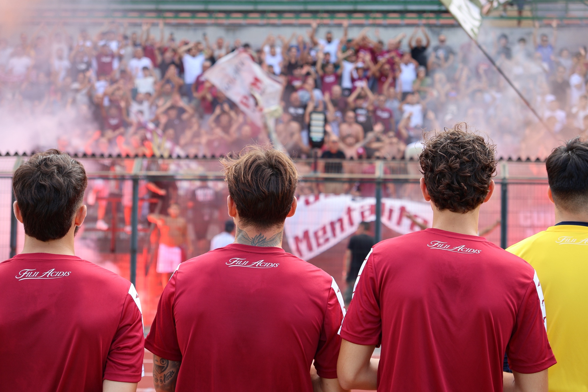 Giocatori dell’Acireale FC di spalle, con il motto Filii Acidis sulla maglia, davanti alla curva granata